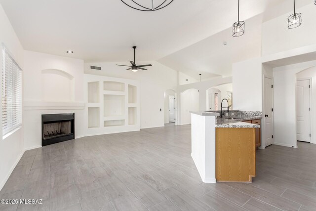 kitchen featuring a sink, visible vents, ceiling fan, arched walkways, and a fireplace