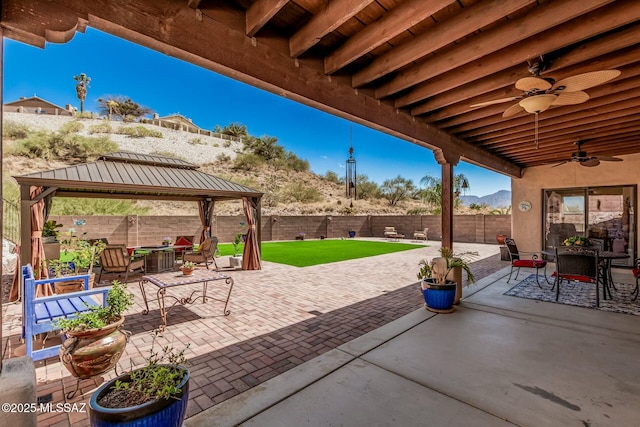 view of patio / terrace with a gazebo, a fenced backyard, a mountain view, outdoor dining area, and a ceiling fan