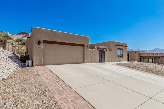 pueblo-style house featuring a garage, stucco siding, fence, and concrete driveway