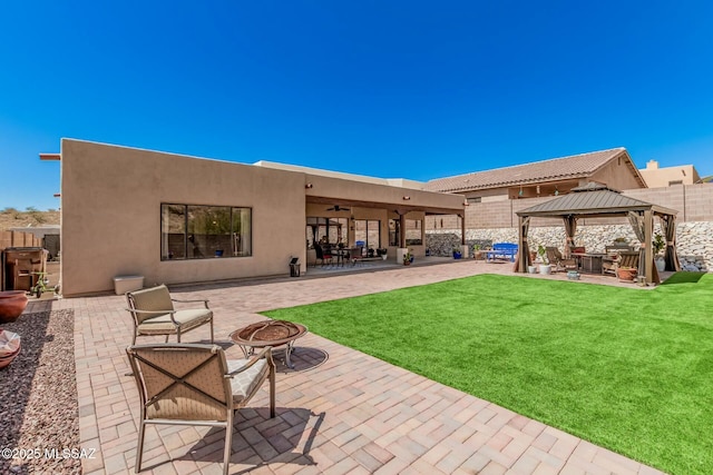rear view of property with a lawn, a gazebo, a fire pit, and a patio area