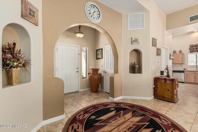 entryway with visible vents, baseboards, a towering ceiling, and light tile patterned floors