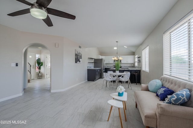 living area with visible vents, baseboards, arched walkways, vaulted ceiling, and ceiling fan with notable chandelier