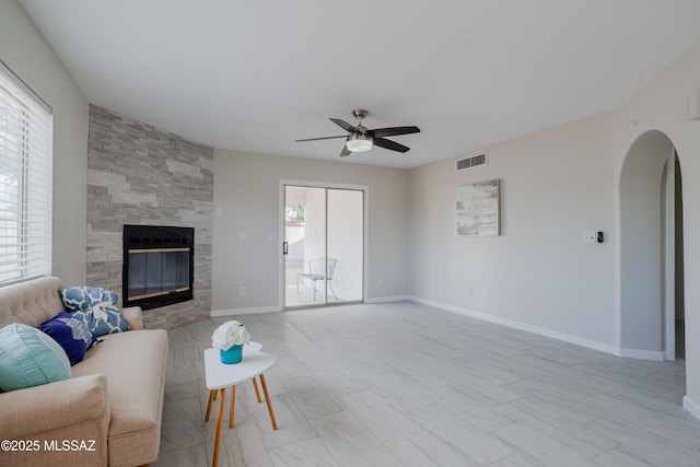 living room featuring visible vents, baseboards, arched walkways, a tile fireplace, and a ceiling fan