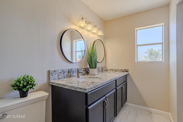 bathroom with marble finish floor, toilet, double vanity, and a sink