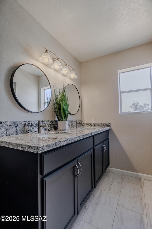 full bathroom with double vanity, baseboards, marble finish floor, and a sink