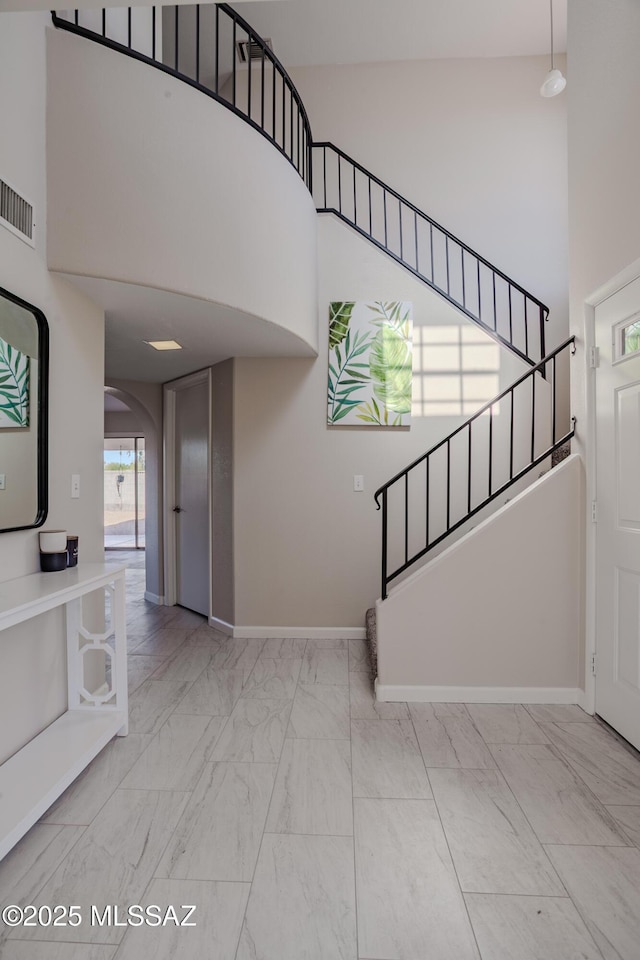 staircase featuring a high ceiling, marble finish floor, visible vents, baseboards, and arched walkways