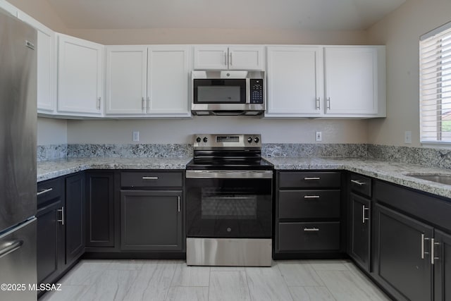 kitchen with light stone countertops, marble finish floor, white cabinets, and stainless steel appliances