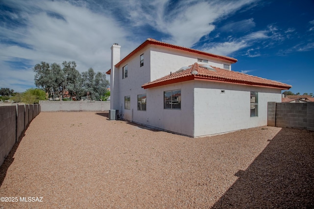 view of side of property featuring a chimney, a fenced backyard, stucco siding, a tiled roof, and central AC