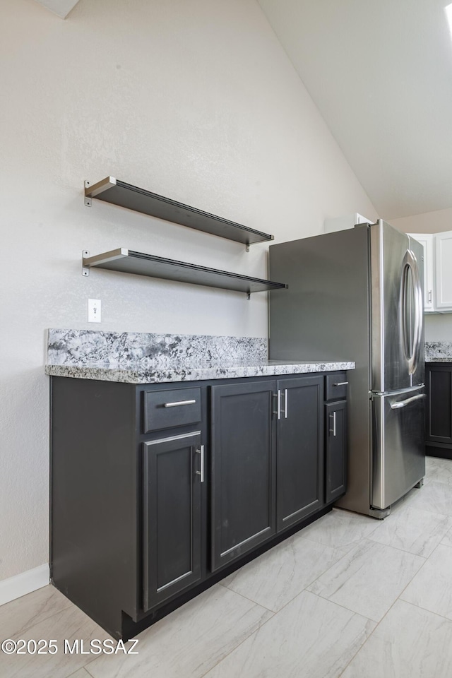 kitchen with light stone countertops, open shelves, marble finish floor, vaulted ceiling, and freestanding refrigerator