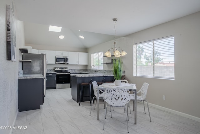 kitchen with a sink, vaulted ceiling with skylight, stainless steel appliances, a peninsula, and light countertops
