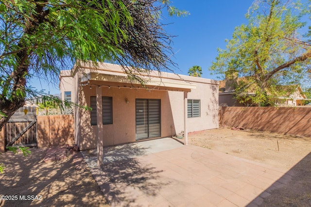 rear view of property with fence, a gate, a patio area, and stucco siding