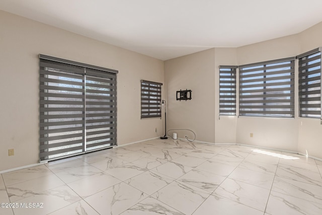 spare room with baseboards, marble finish floor, and a wealth of natural light