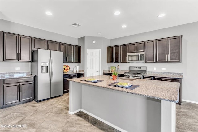 3156 S Three D Ct, Tucson, AZ 85713 - kitchen featuring appliances with stainless steel finishes, dark brown cabinetry, light stone countertops, a center island with sink, and baseboards