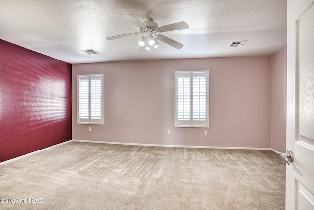 carpeted spare room featuring visible vents, baseboards, and ceiling fan