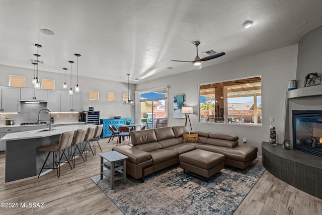 living room with a large fireplace, visible vents, light wood-style flooring, and a ceiling fan