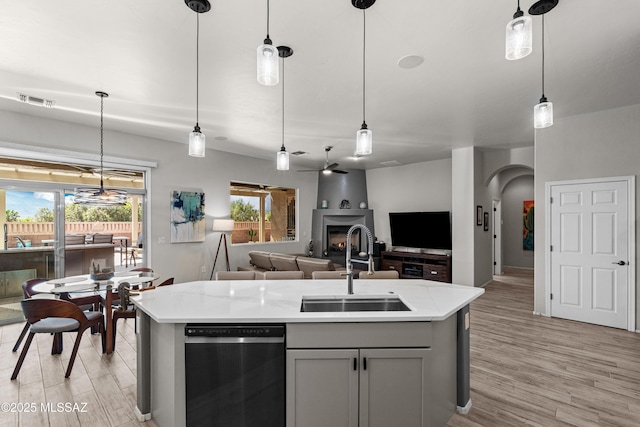 kitchen with a sink, light wood-type flooring, gray cabinets, stainless steel dishwasher, and arched walkways