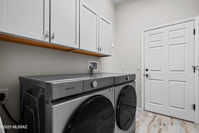 clothes washing area featuring cabinet space, washing machine and dryer, and light wood-type flooring