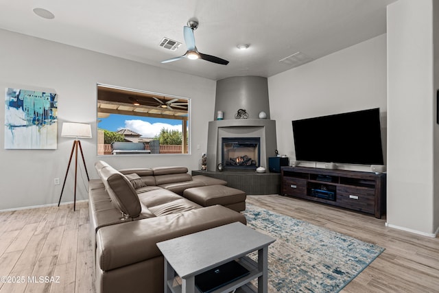 living area with visible vents, wood finished floors, a ceiling fan, and a glass covered fireplace