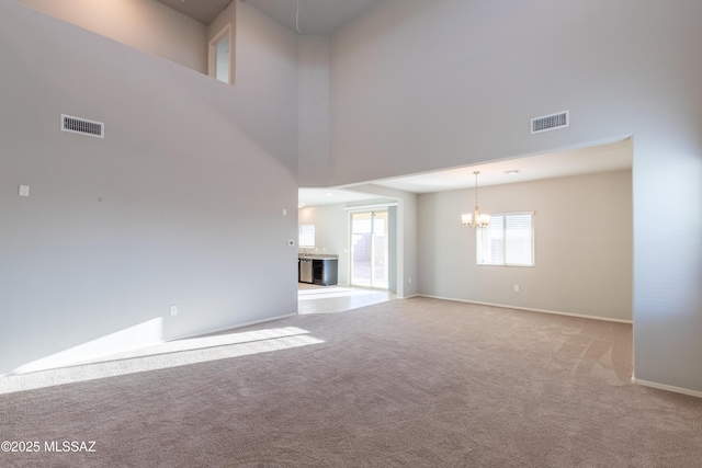 unfurnished living room featuring a high ceiling, carpet, a notable chandelier, and visible vents