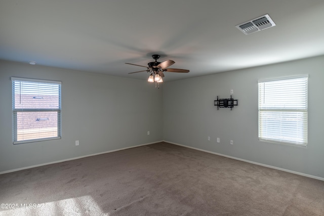 empty room with plenty of natural light, a ceiling fan, carpet flooring, and visible vents