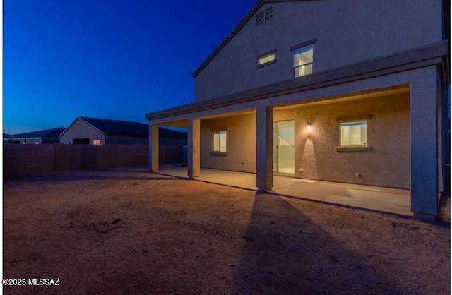 back of house at night featuring a patio, a fenced backyard, and stucco siding