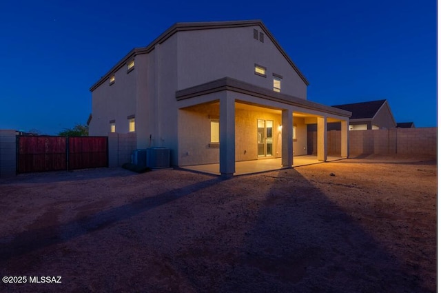 back of house at twilight featuring central air condition unit, a fenced backyard, a patio area, and stucco siding