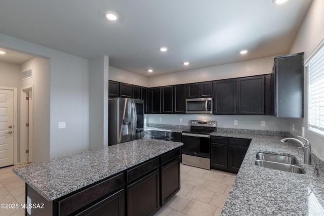kitchen with a kitchen island, light tile patterned floors, appliances with stainless steel finishes, and a sink