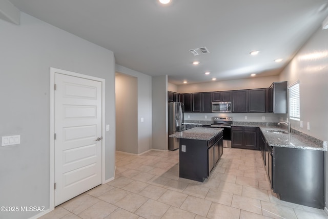 kitchen with a kitchen island, stainless steel appliances, light stone counters, and a sink