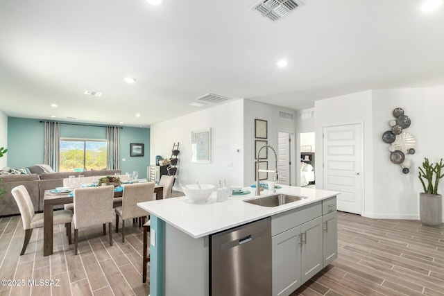 kitchen with gray cabinets, stainless steel dishwasher, a sink, visible vents, and open floor plan