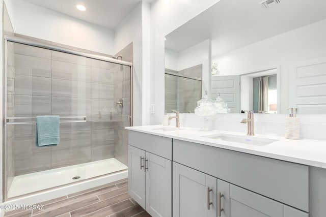full bath featuring visible vents, a shower stall, double vanity, and a sink