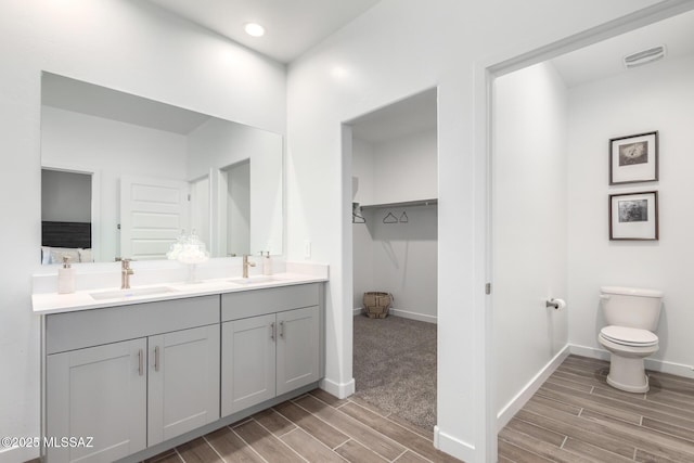bathroom featuring a sink, double vanity, visible vents, baseboards, and wood finish floors
