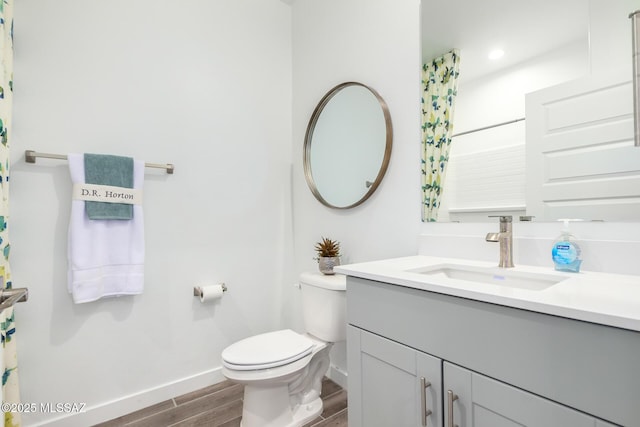 bathroom with wood finished floors, toilet, vanity, and baseboards