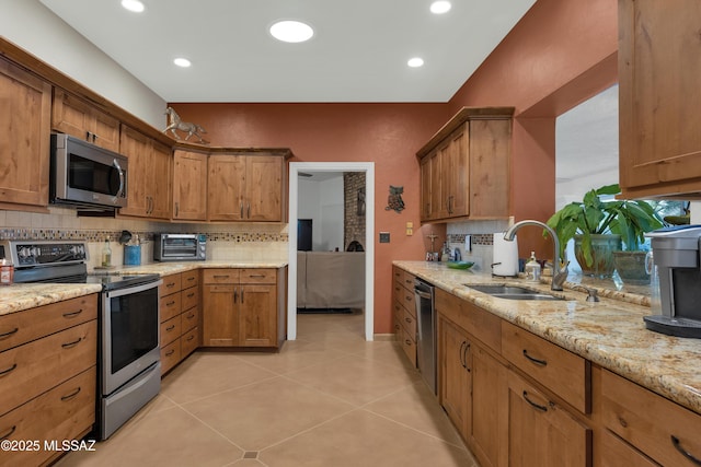 kitchen with backsplash, appliances with stainless steel finishes, brown cabinets, a sink, and light tile patterned floors