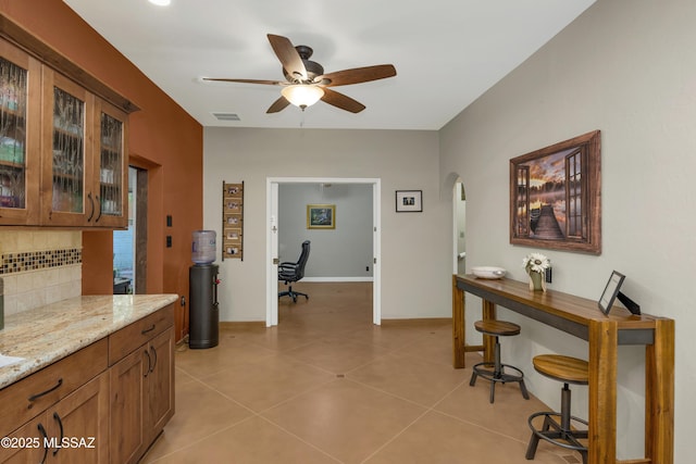 interior space with ceiling fan, decorative backsplash, visible vents, arched walkways, and light stone countertops