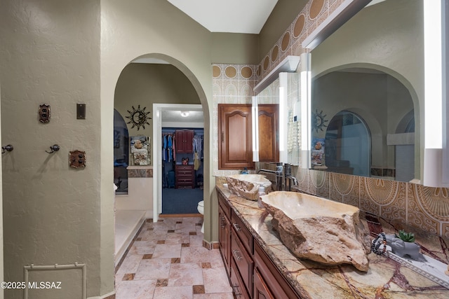 bathroom with vanity, a textured wall, stone finish floor, and toilet