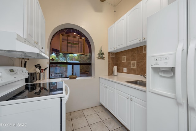 kitchen with a sink, under cabinet range hood, white cabinets, and white appliances
