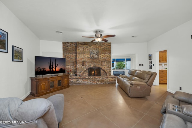 living area with tile patterned flooring, a ceiling fan, a brick fireplace, and visible vents