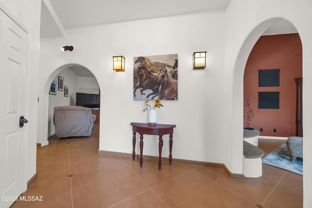 hallway featuring baseboards, arched walkways, and tile patterned floors