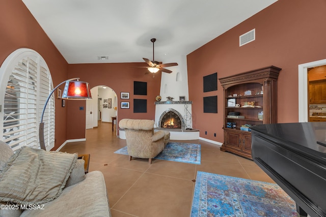 living room featuring ceiling fan, arched walkways, a large fireplace, light tile patterned floors, and visible vents