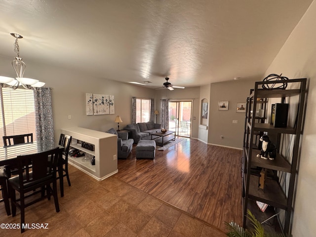 living room featuring baseboards, ceiling fan with notable chandelier, and a textured ceiling