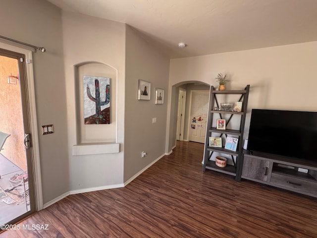 unfurnished living room featuring arched walkways, wood finished floors, and baseboards