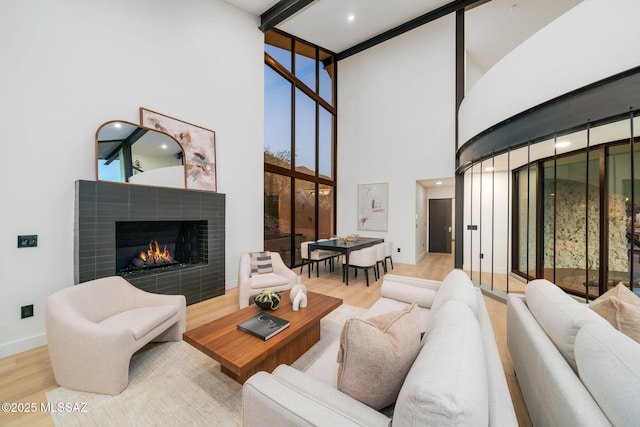 living area with baseboards, recessed lighting, a towering ceiling, wood finished floors, and a tiled fireplace