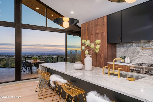 kitchen featuring light stone counters, decorative backsplash, a sink, a kitchen bar, and modern cabinets