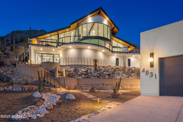 art deco inspired home with stairs, a garage, stucco siding, and a balcony