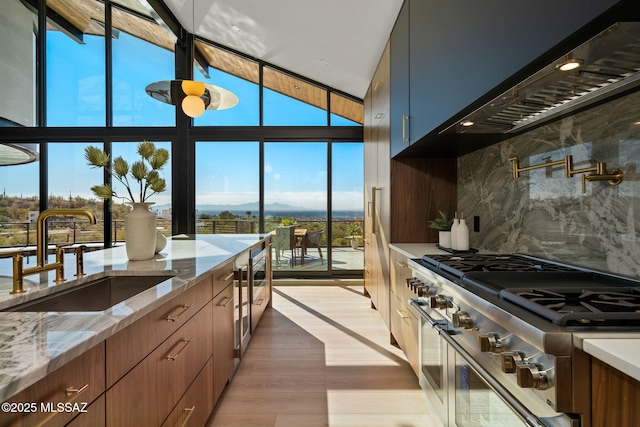 kitchen with expansive windows, decorative backsplash, double oven range, wall chimney range hood, and a sink
