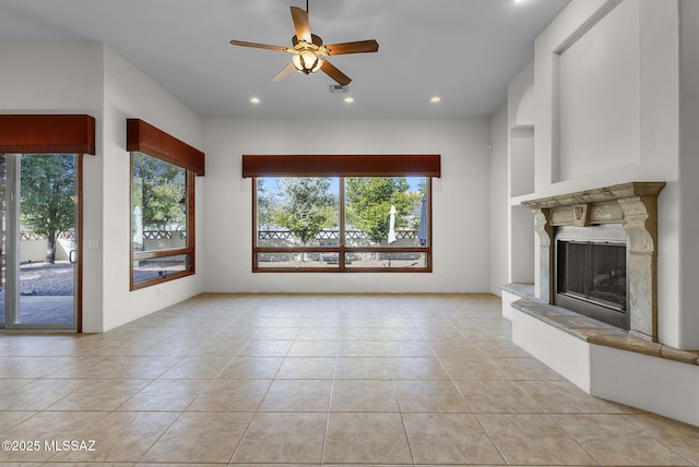 unfurnished living room featuring a high end fireplace, plenty of natural light, a ceiling fan, and light tile patterned flooring