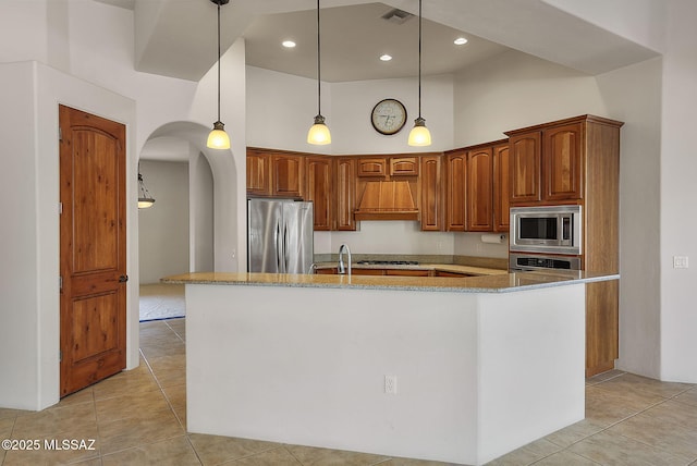 kitchen with appliances with stainless steel finishes, light stone counters, high vaulted ceiling, visible vents, and a center island with sink