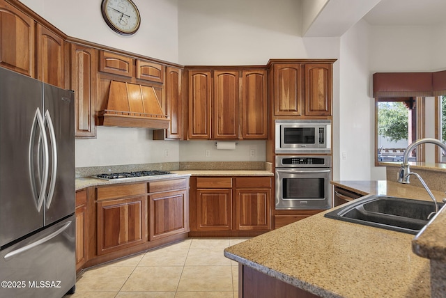 kitchen with a sink, brown cabinetry, stainless steel appliances, light tile patterned floors, and custom exhaust hood