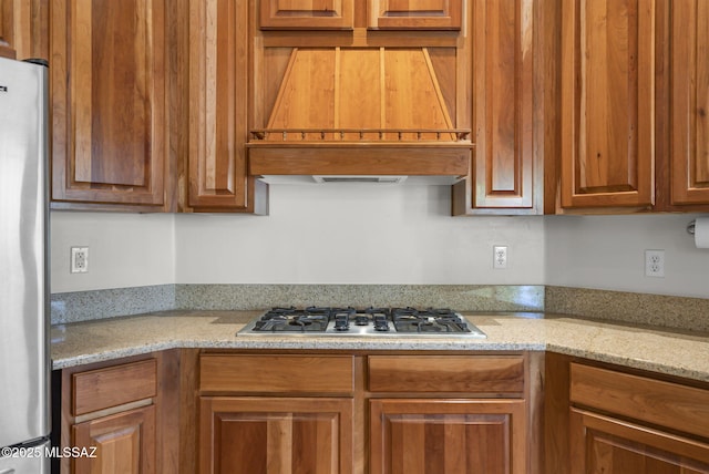 kitchen featuring premium range hood, brown cabinetry, stainless steel appliances, and light stone countertops