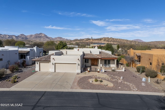 pueblo-style home featuring stucco siding, concrete driveway, a mountain view, and a garage